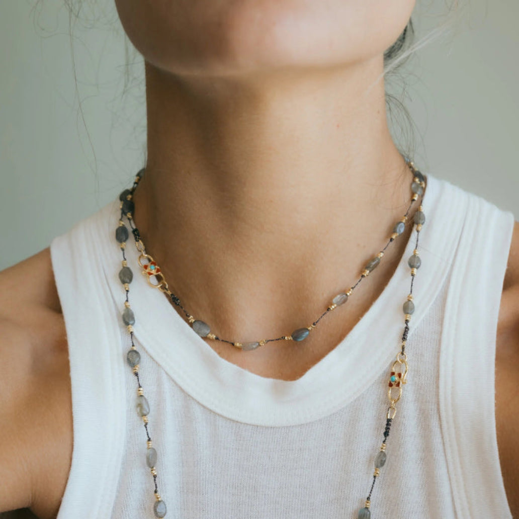 Necklace with gray beads and gold accents worn by a person in a white top.