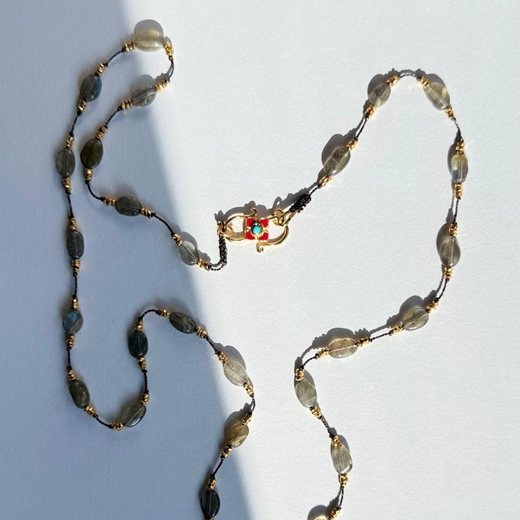 Necklace with gray beads and gold accents worn by a person in a white top.