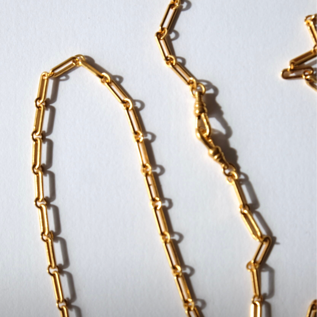 Gold chain necklace worn by a person in a white lace top against a neutral background
