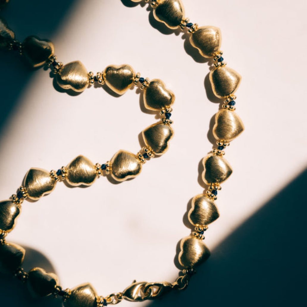 Gold necklace with heart-shaped beads on a light background